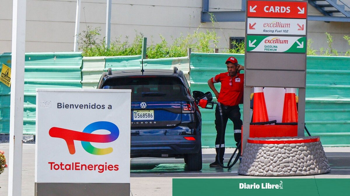 Empleado de gasolinera dominicana despachando combustible junto a surtidores con precios
