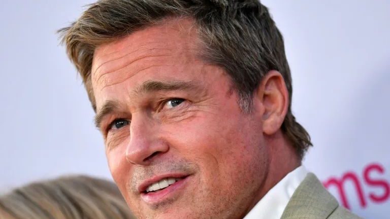 Brad Pitt en alfombra roja con traje oscuro, sonriendo ante los medios