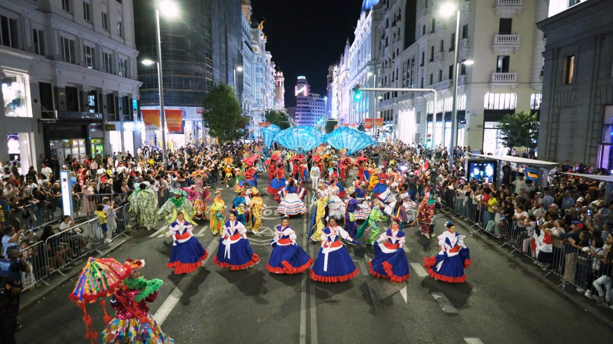 Delegación dominicana con trajes de carnaval y la bandera nacional desfilando en la Gran Vía de Madrid durante la Cabalgata de la Hispanidad