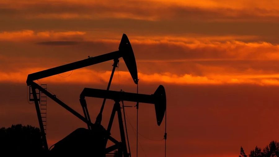 Trabajadores en plataforma petrolera con barriles de crudo al fondo, en referencia a la caída de la demanda mundial de petróleo