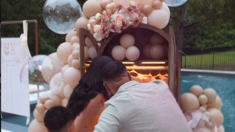 DJ Adoni y su pareja frente a un armario vintage del que sale humo rosado durante el gender reveal de su bebé