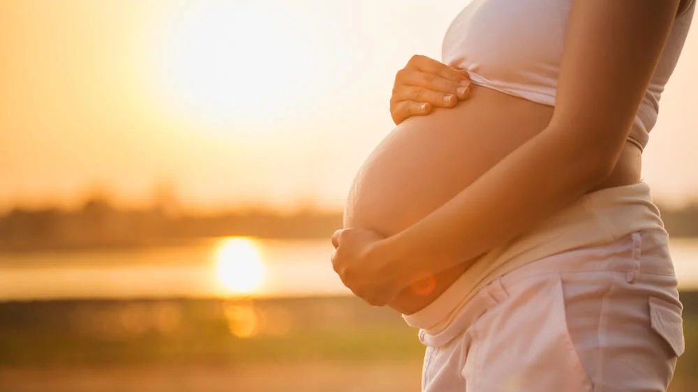 Mujer embarazada con vientre visible sentada en consulta médica junto a profesional de salud