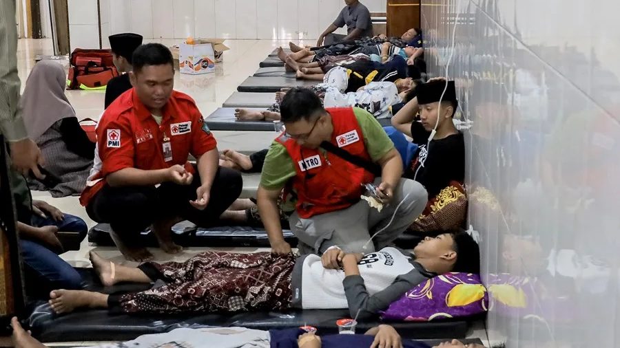 Estudiantes indonesios recibiendo atención médica sobre colchonetas en el suelo tras brote de intoxicación alimentaria en internado de Java Oriental