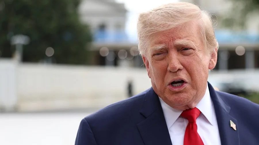 Donald Trump hablando ante micrófonos con bandera de EE.UU. al fondo