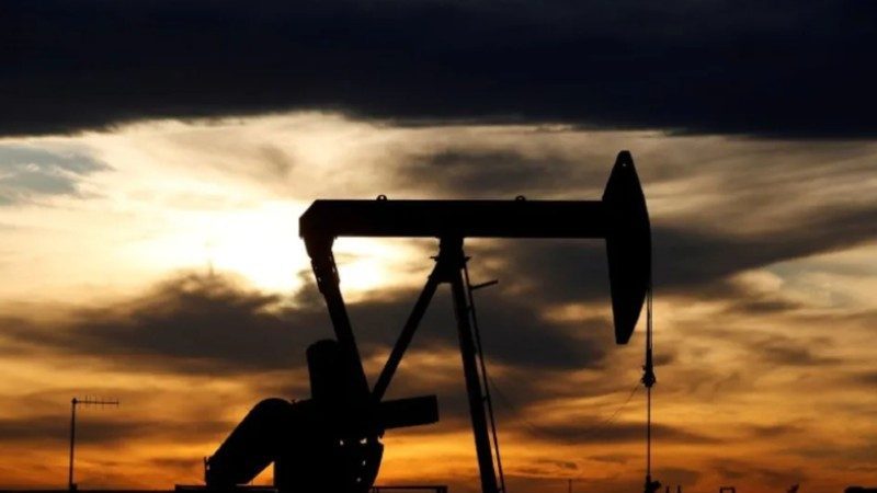 Barriles de petróleo apilados en una refinería con gráfica de precios en caída al fondo