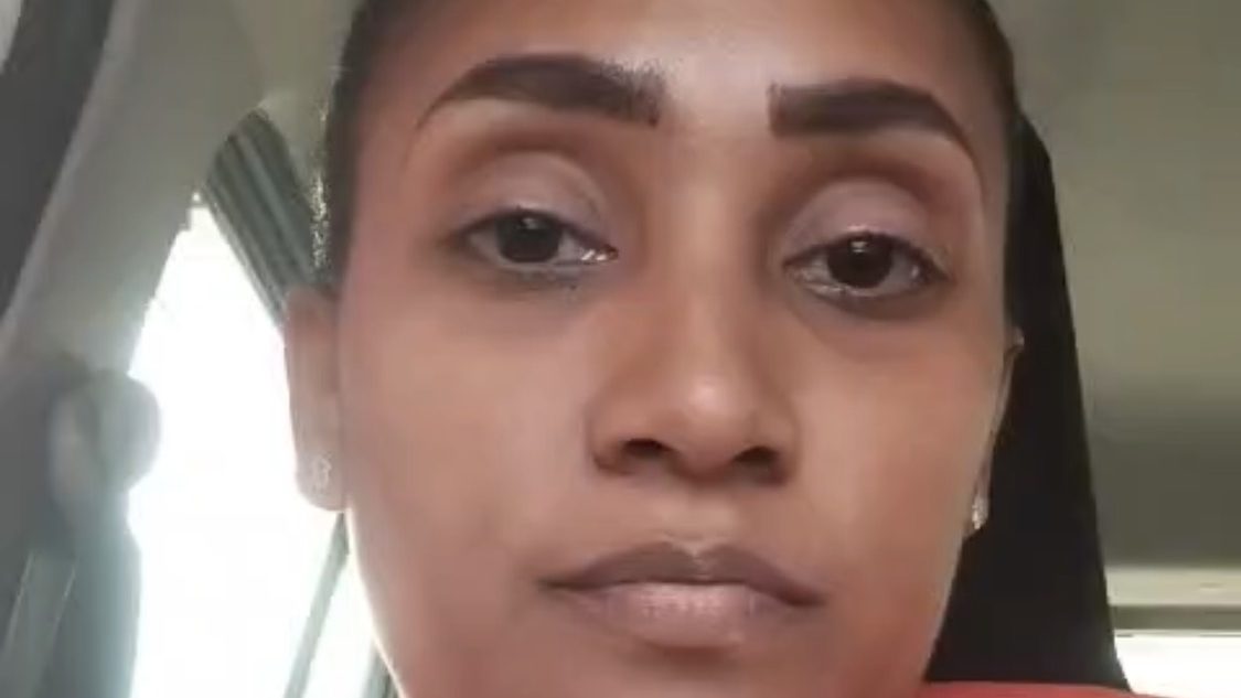 Mujer dominicana frente a oficinas de institución pública esperando respuesta sobre pago de prestaciones laborales