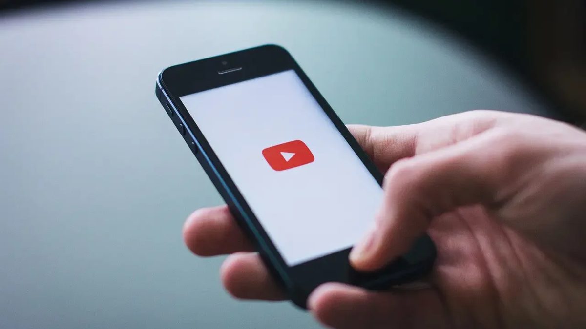Pantalla de YouTube abierta en un celular junto a un control remoto de televisión, representando la regulación de contenido digital