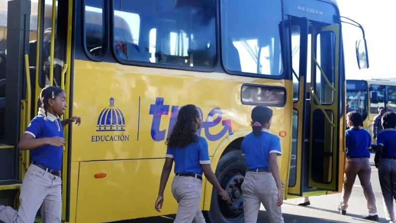 Autobuses del TRAE alineados frente a un centro educativo público en República Dominicana al inicio del año escolar