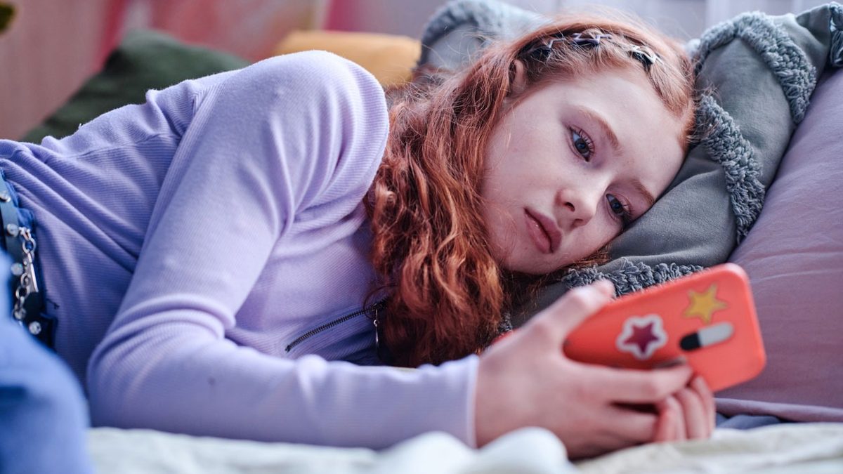Joven mirando su reflejo en el espejo mientras sostiene un teléfono con redes sociales abiertas