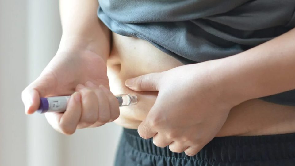 Médico sosteniendo un medicamento GLP-1 como Ozempic junto a una mujer en consulta posparto